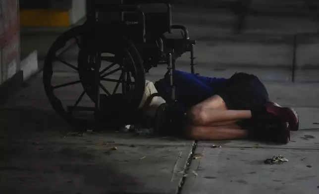 A homeless person sleeps under a wheelchair alongside a parking garage in deserted downtown Tampa, Fla., during the approach of Hurricane Milton, Wednesday, Oct. 9, 2024. (AP Photo/Rebecca Blackwell)