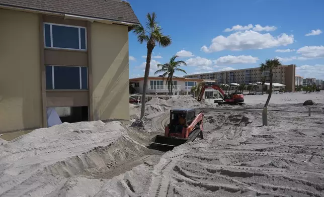 Scott Bennett, a contractor who specializes in storm recovery, drives a skid steer as he removes sand around 5 feet deep from the patio of a beachfront condominium in Venice, Fla., following the passage of Hurricane Milton, Saturday, Oct. 12, 2024. (AP Photo/Rebecca Blackwell)