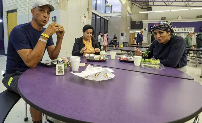 Muhamed Aftah, Fatimah Aftah and Senna Aftah eat a meal at a hurricane shelter at River Ridge Middle/High School in preparation for Hurricane Milton, Wednesday, Oct. 9, 2024, in New Port Richey, Fla. (AP Photo/Mike Carlson)