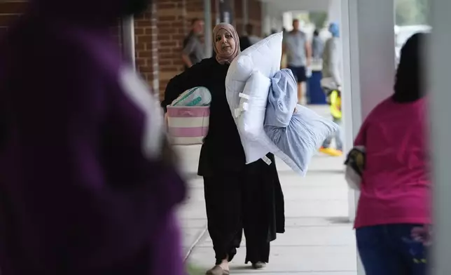 A woman carries pillows and supplies into Gibbs High School, a government storm shelter where 1700 people had already sought shelter by late morning, ahead of the arrival Hurricane Milton, in St. Petersburg, Fla., Wednesday, Oct. 9, 2024. (AP Photo/Rebecca Blackwell)