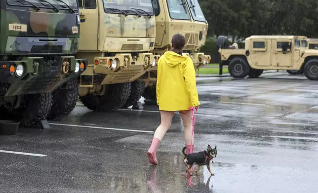 Erin Ferguson walks her dog while looking at equipment stationed by the Florida National Guard in preparation for Hurricane Milton, Wednesday, Oct. 9, 2024, in New Port Richey, Fla. (AP Photo/Mike Carlson)