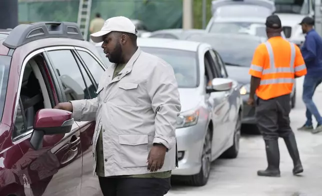 North Miami Beach, Fla., commissioner McKenzie Fleurimond, left, checks cars as residents line up to receive sandbags from the city to help prevent flooding, as Hurricane Milton prepares to strike Florida, Tuesday, Oct. 8, 2024, in North Miami Beach. (AP Photo/Wilfredo Lee)