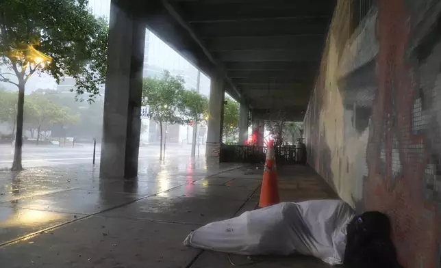 Melvin Lee Hicks, who is homeless, lies under a sheet donated by a nearby hotel, as he shelters alongside a parking garage in downtown Tampa, Fla., during the approach of Hurricane Milton, Wednesday, Oct. 9, 2024. (AP Photo/Rebecca Blackwell)