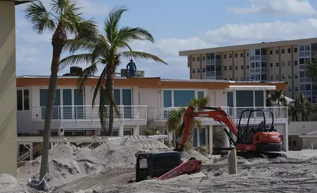 Scott Bennett, a contractor who specializes in storm recovery, drives a skid steer, bottom, as he removes sand around 5 feet deep from the patio of a beachfront condominium in Venice, Fla., following the passage of Hurricane Milton, Saturday, Oct. 12, 2024. Bennett said he had just finished digging out the same condominium complex after Hurricane Helene, when Milton buried it in an even deeper layer of sand. Before Helene hit, the Venice native said, he'd "never seen sand like this. Wind rain, water, but never sand." (AP Photo/Rebecca Blackwell)