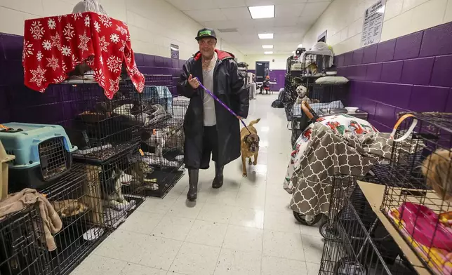 Logan Smith takes his dog Zak through some of the 283 registered pets in the evacuation shelter at River Ridge Middle/High School in preparation for Hurricane Milton on Wednesday, Oct. 9, 2024, in New Port Richey, Fla. (AP Photo/Mike Carlson)