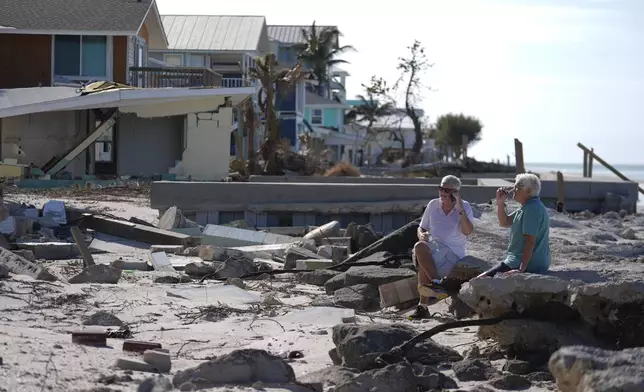 Property owners who preferred not to be named sit on the torn-up beach near their beachfront home and business, which was damaged in Hurricane Helene and then destroyed in Hurricane Milton, on Manasota Key, in Englewood, Fla., following the passage of Hurricane Milton, Sunday, Oct. 13, 2024. (AP Photo/Rebecca Blackwell)