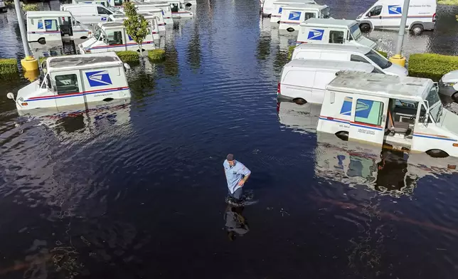 A USPS worker inspects trucks that had been relocated to protect them from wind but which are now underwater as intense rain from Hurricane Milton caused the Anclote River to flood, Friday, Oct. 11, 2024, in New Port Richey, Fla. (AP Photo/Mike Carlson)