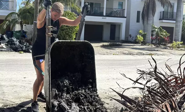 Jen Hilliard dumps sandy muck from a wheelbarrow in the aftermath of Hurricane Milton on Saturday, Oct. 12, 2024, outside a friend’s house in Bradenton Beach, Fla. (AP Photo/Russ Bynum)