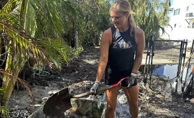 Jen Hilliard shovels sandy muck into a wheelbarrow outside a friend’s house after Hurricane Milton, Saturday, Oct. 12, 2024, in Bradenton Beach, Fla. (AP Photo/Russ Bynum)