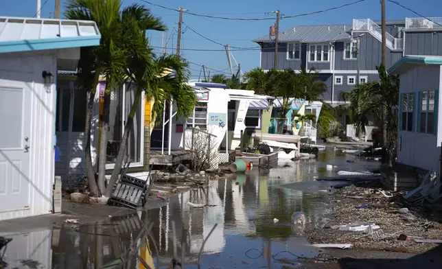 Water left by Hurricane Milton floods a road inside Pines Trailer Park, where debris was still piled outside homes from Hurricane Helene, in Bradenton Beach on Anna Maria Island, Fla., Thursday, Oct. 10, 2024. (AP Photo/Rebecca Blackwell)