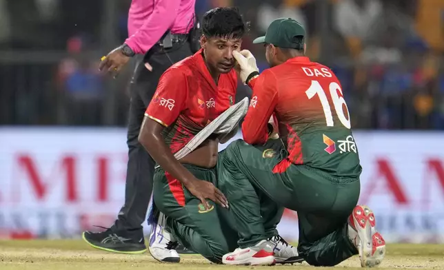 Bangladesh's Mustafizur Rahman, left, gets his left eye examined by teammate Litton Das after some foreign body entered his eye during the first T20 cricket match between Bangladesh and India in Gwalior, India, Sunday, Oct. 6, 2024. (AP Photo/Manish Swarup)