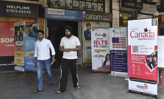 People walk past banners inviting students to study in Canada and other places abroad at a market in Amritsar, in the northern Indian state of Punjab, Tuesday, Oct. 15, 2024. (AP Photo/Prabhjot Gill)