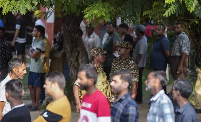 Paramilitary soldiers guard as people queue up to cast their vote at a polling booth during the final phase of an election to choose a local government in Indian-controlled Kashmir, in Jammu, India, Tuesday, Oct.1, 2024. (AP Photos/Channi Anand)