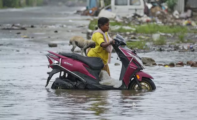 A woman drags a two wheeler with her pet on it through a flooded street after heavy rains in Chennai, India, Wednesday, Oct.16, 2024. (AP Photo/Mahesh Kumar A.)