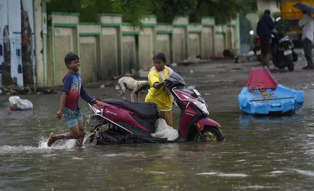 A woman drags a two wheeler with her pet on it, through a flooded street after heavy rains in Chennai, India, Wednesday, Oct.16, 2024. (AP Photo/Mahesh Kumar A.)