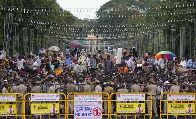 People stand behind barricades to watch a procession on the last day of the Dussehra festivities, in Mysuru, India, Saturday, Oct. 12, 2024. (AP Photo/Aijaz Rahi)