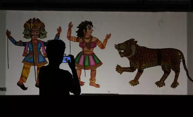 A boy films leather puppets, used in a shadow play, on display at a theater during the Dussehra festivities, in Mysuru, India, Saturday, Oct. 12, 2024. (AP Photo/Aijaz Rahi)