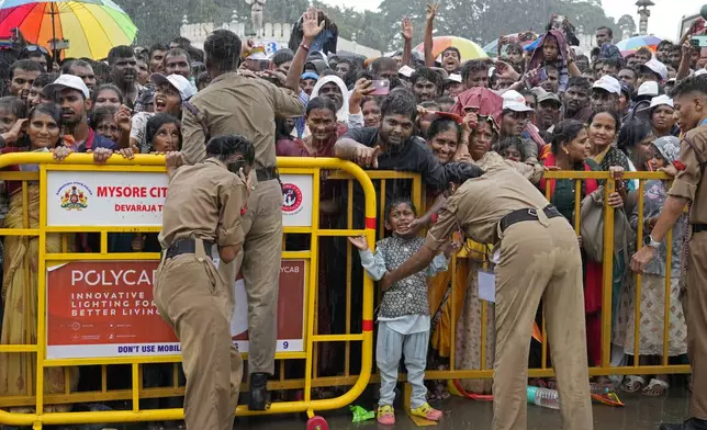 A military cadet tries to calm down a crying child who was waiting with his elders for hours during rains to watch a procession on the last day of the Dussehra festivities, in Mysuru, India, Saturday, Oct. 12, 2024. (AP Photo/Aijaz Rahi)