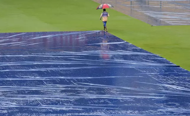 A groundsman walks past the pitch area covered with plastic sheets after rains delayed the start of the day one of the first cricket test match between India and New Zealand at the M.Chinnaswamy Stadium, in Bengaluru, India, Wednesday, Oct. 16, 2024. (AP Photo/Aijaz Rahi)