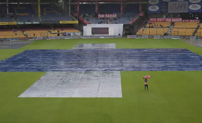 A groundsman walks past the pitch area covered with plastic sheets after rains delayed the start of the day one of the first cricket test match between India and New Zealand at the M.Chinnaswamy Stadium, in Bengaluru, India, Wednesday, Oct. 16, 2024. (AP Photo/Aijaz Rahi)