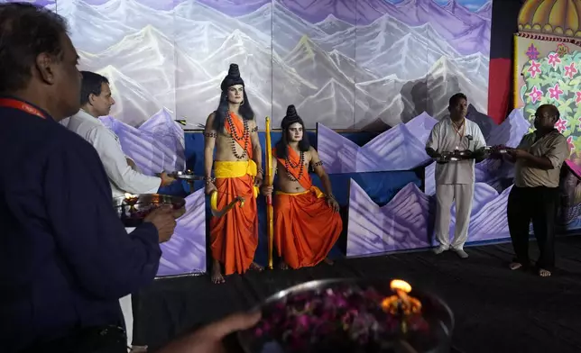 Two actors who played Hindu god Rama, sitting, and his brother Laxman, standing next to him in the center, wait on the stage at the end of the third day of Ramleela, a dramatic folk re-enactment of the life of Rama according to the ancient Hindu epic Ramayana, as event organizers and donors pray to them, in New Delhi, India, Wednesday, Oct. 9, 2024. (AP Photo/Manish Swarup)