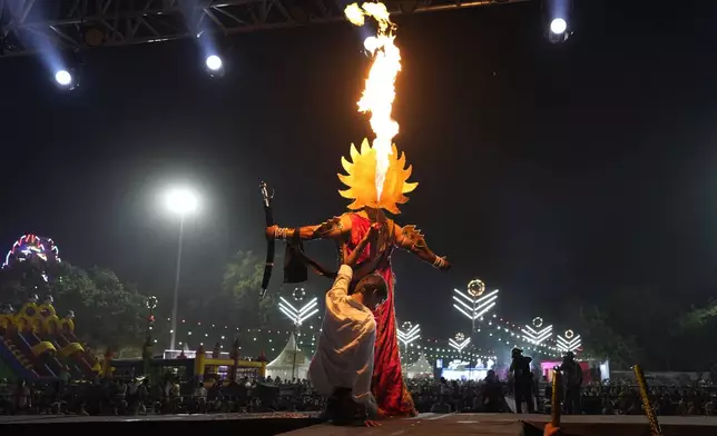 A production assistant holds a fire stick sitting behind Vikas Sirswal, 32, who is playing the demon king Ravana onstage, during Ramleela, a dramatic folk re-enactment of the life of Hindu god Rama according to the ancient Hindu epic Ramayana, in New Delhi,India, Wednesday, Oct. 9, 2024. (AP Photo/Manish Swarup)