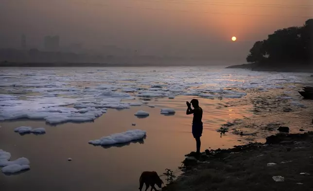 A person prays on the banks of the river Yamuna as toxic foams float in the river, in New Delhi, India, Tuesday, Oct. 29, 2024. (AP Photo/Manish Swarup)