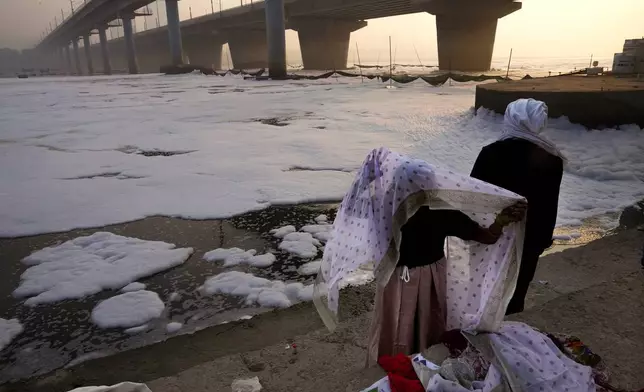 An elderly woman changes her clothes after praying in the river Yamuna filled with toxic foams in New Delhi, India, Tuesday, Oct. 29, 2024. (AP Photo/Manish Swarup)