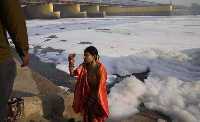 A woman in traditional attire gets photographed in front of the river Yamuna filled with toxic foams in New Delhi, India, Tuesday, Oct. 29, 2024. (AP Photo/Manish Swarup)