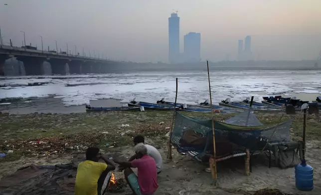 Worker warm themselves in front of a bonfire sitting on the banks of the river Yamuna as toxic foam floats, in New Delhi, India, Tuesday, Oct. 29, 2024. (AP Photo/Manish Swarup)