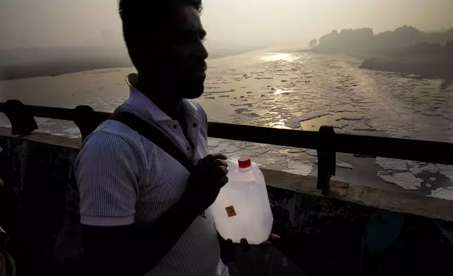 A person carries sacred Ganges river water in a container as he walks across the bridge over the river Yamuna filled with toxic foams in New Delhi, India, Tuesday, Oct. 29, 2024. (AP Photo/Manish Swarup)