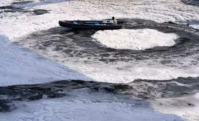 A worker for the Delhi Jal or water board moves his boat in circular pattern to cut the flow of toxic foams flowing in the river Yamuna in New Delhi, India, Tuesday, Oct. 29, 2024. (AP Photo/Manish Swarup)