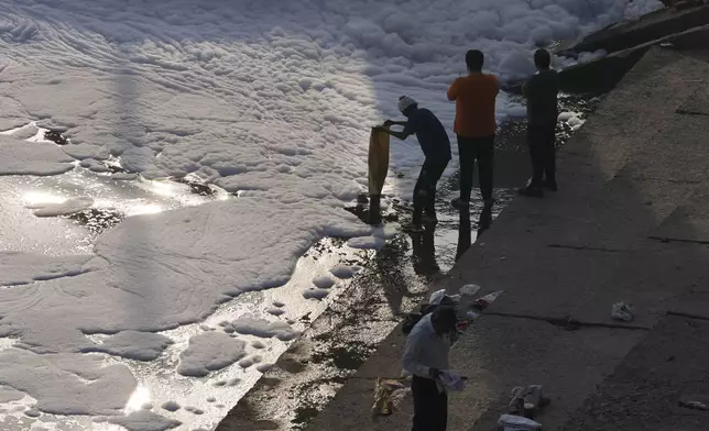 A person empties a bag of garbage in the the river Yamuna filled with toxic foams in New Delhi, India, Tuesday, Oct. 29, 2024. (AP Photo/Manish Swarup)