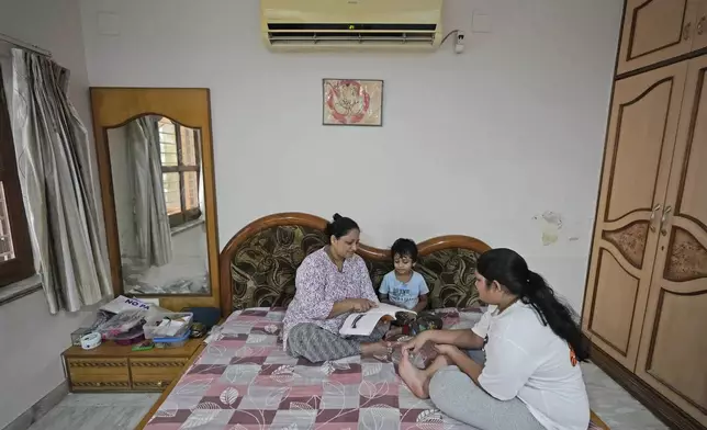 Archana Patil, 40, her son Darsh Patil, 5, and daughter Bhavya Patil, 13, sit under a Voltas air conditioner, a Tata group product, at home in Ahmedabad, India, Thursday, Oct. 10, 2024. (AP Photo/Ajit Solanki)