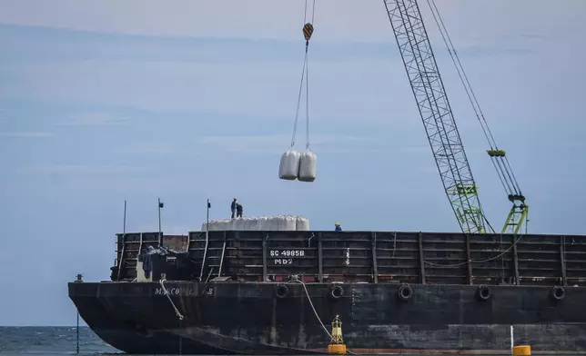 Workers load sacks of wood pellets onto a barge at a port in Pohuwato, Gorontalo province, Indonesia, Tuesday, Oct. 22, 2024. (AP Photo/Yegar Sahaduta Mangiri)