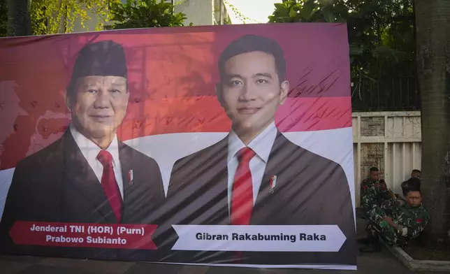 Soldiers sit next to a banner showing Indonesian President-elect Prabowo Subianto, left, and Vice President-elect Gibran Rakabuming Raka, who is also the eldest son of outgoing President Joko Widodo in Jakarta, Indonesia, Sunday, Oct. 20, 2024. (AP Photo/Dita Alangkara)