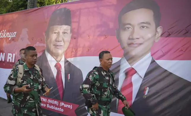 Soldiers walk in front of a banner showing Indonesian President-elect Prabowo Subianto, left, and Vice President-elect Gibran Rakabuming Raka, who is also the eldest son of outgoing President Joko Widodo, in Jakarta, Indonesia, Sunday, Oct. 20, 2024. (AP Photo/Dita Alangkara)