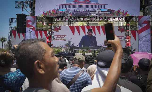 An Indonesia take picture with his cellphone as others watch from a giant screen of Newly-inaugurated Indonesian President Prabowo Subianto speech in Jakarta, Indonesia, Sunday, Oct. 20, 2024. (AP Photo/Dita Alangkara)