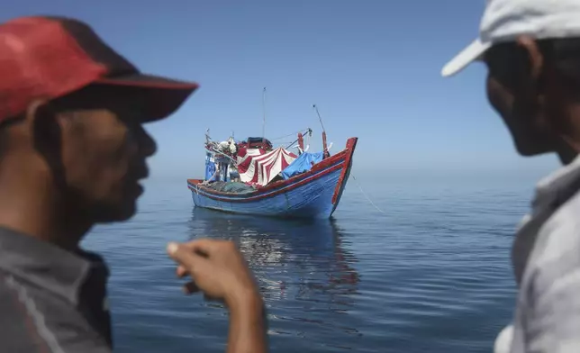 Acehnese men inspect a boat carrying Rohingya refugees anchored in the waters near the coast of Labuhan Haji, Aceh province, Indonesia, Tuesday, Oct. 22, 2024. (AP Photo/Binsar Bakkara)