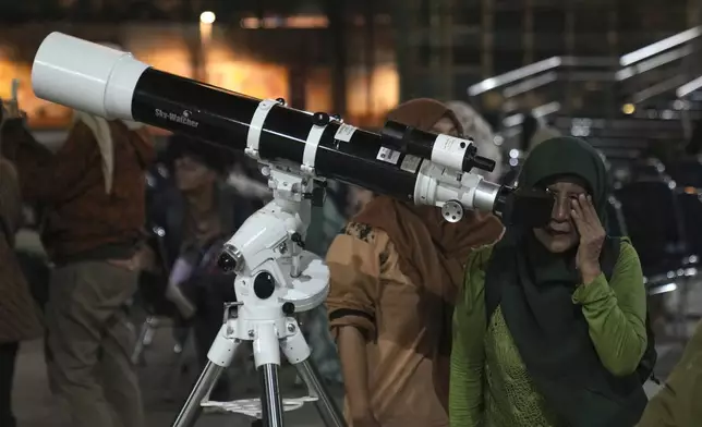 A woman uses a telescope provided by Planetarium Jakarta to watch the moon rising, in Jakarta, Indonesia, Thursday, Oct. 17, 2024. (AP Photo/Dita Alangkara)