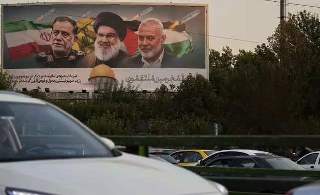 Vehicles drive past a billboard on a highway in Tehran, Iran, Monday, Oct. 7, 2024, showing slain Hezbollah leader Hassan Nasrallah, center, late Hamas leader Ismail Haniyeh, right, and the late Iranian Revolutionary Guard Gen. Abbas Nilforushan, who was killed in an Israeli airstrike. The billboard contains a verse of Quran that reads: "We will surely inflict punishment upon the wicked." (AP Photo/Vahid Salemi)