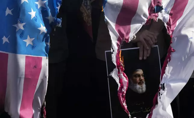 A representation of the U.S. flag is set on fire as a demonstrator holds a poster of slain Hezbollah leader Hassan Nasrallah in a rally commemorating him, in Tehran, Iran, Wednesday, Oct. 2, 2024. (AP Photo/Vahid Salemi)