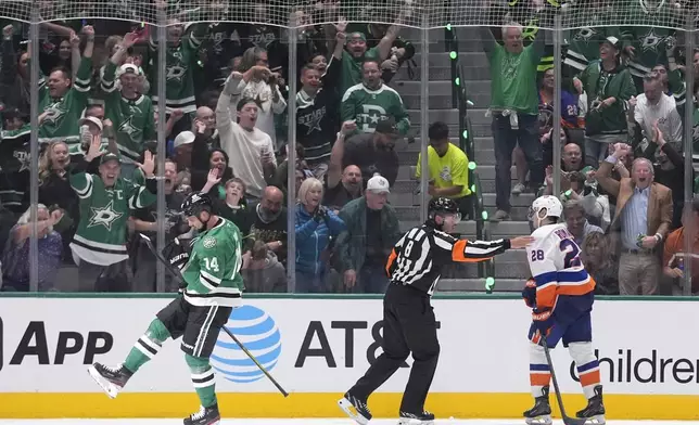 Dallas Stars left wing Jamie Benn (14) celebrates his goal as New York Islanders defenseman Alexander Romanov (28) looks on with referee Francois St. Laurent (8) calling the goal good during the second period of an NHL hockey game, Saturday, Oct. 12, 2024, in Dallas. (AP Photo/LM Otero)