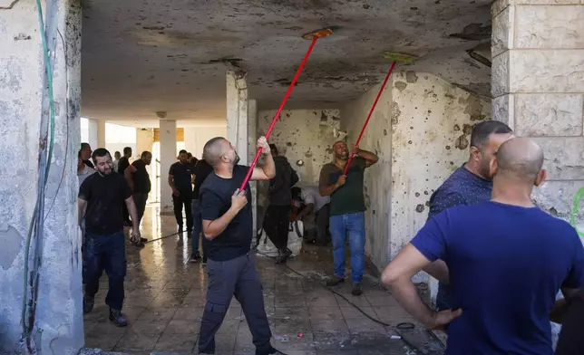 Neighbors clean blood stains from the ceiling of a damaged house where one person was killed after a projectile launched from Lebanon slammed into Maalot-Tarshiha, northern Israel, Tuesday, Oct. 29, 2024. (AP Photo/Ohad Zwigenberg)