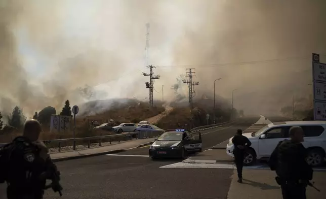 Israeli police officers stand next to a site of a fire after a rocket, fired from Lebanon, hit an area near the town of Rosh Pinna, northern Israel, Sunday, Oct. 20, 2024. (AP Photo/Leo Correa)