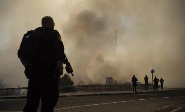 Israeli police officers stand next to a site of a fire after a rocket, fired from Lebanon, hit an area near the town of Rosh Pinna, northern Israel, Sunday, Oct. 20, 2024. (AP Photo/Leo Correa)