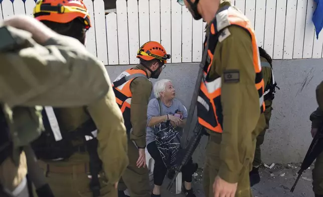 Israeli soldiers from the Homefront Command unit treat an elderly woman at the site that was hit by a rocket fired from Lebanon, in Kiryat Yam, northern Israel, on Tuesday, Oct. 8, 2024. (AP Photo/Ariel Schalit)