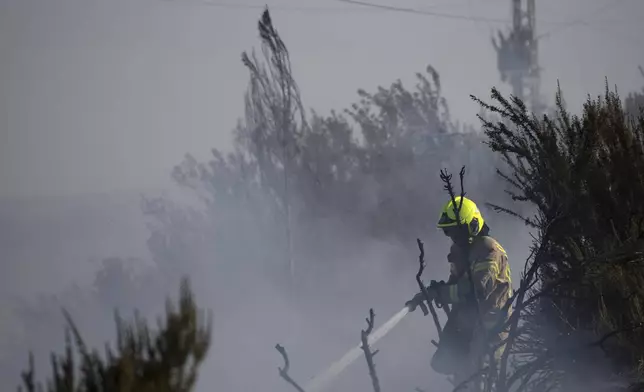 A firefighter works to extinguish a fire after a rocket, fired from Lebanon, hit an area next to a road near Kiryat Shmona, northern Israel, Saturday, Oct. 5, 2024. (AP Photo/Leo Correa)