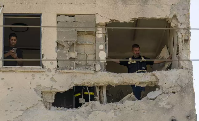 Municipality workers survey the damage to an apartment building struck by a rocket fired from Lebanon, in Kiryat Ata, northern Israel, Saturday, Oct. 19, 2024. (AP Photo/Ariel Schalit)