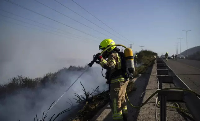 A firefighter works to extinguish a fire after a rocket, fired from Lebanon, hit an area next to a road near Kiryat Shmona, northern Israel, Saturday, Oct. 5, 2024. (AP Photo/Leo Correa)